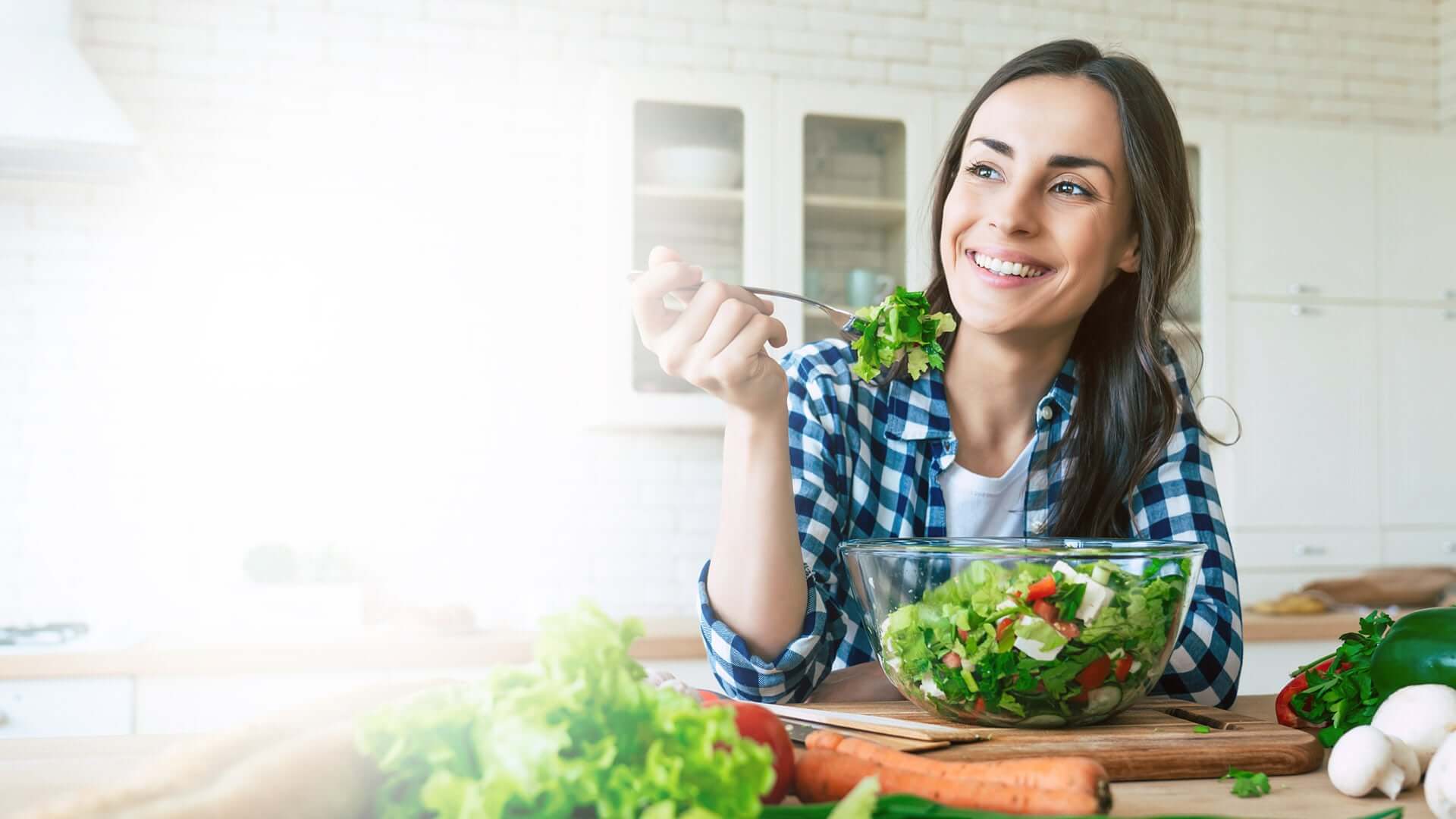 portrait of happy beautiful young woman while she try tasty vegan salad in the kitchen at home